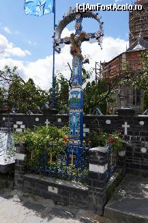 [P03] Crucea din afara cimitirului pe care sunt desenate trei episoade din viața lui Isus iar în partea de jos este desenat un mic drăcușor. În spatele ei este gardul cimitirului iar în spate de tot se vede o parte din biserică, aflată în proces de restaurare. Observați steagul NATO.  » foto by Utube
 - 
<span class="allrVoted glyphicon glyphicon-heart hidden" id="av381562"></span>
<a class="m-l-10 hidden" id="sv381562" onclick="voting_Foto_DelVot(,381562,7494)" role="button">șterge vot <span class="glyphicon glyphicon-remove"></span></a>
<a id="v9381562" class=" c-red"  onclick="voting_Foto_SetVot(381562)" role="button"><span class="glyphicon glyphicon-heart-empty"></span> <b>LIKE</b> = Votează poza</a> <img class="hidden"  id="f381562W9" src="/imagini/loader.gif" border="0" /><span class="AjErrMes hidden" id="e381562ErM"></span>